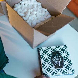 Open cardboard box with packing peanuts and hand placing patterned item.
