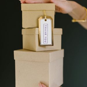 Three kraft gift boxes stacked with a 'Thank You' tag held by a woman's hands.
